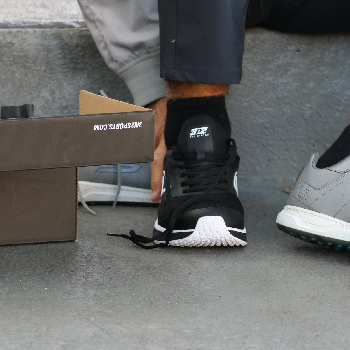 Person wearing black shoes and gray pants on a concrete floor.